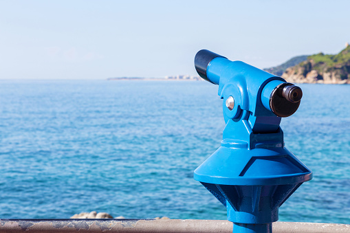 Blue tourist monocular with a beautiful mediterranean landscape in the background on a sunny summer day. Copy space for text.  Selective focus  