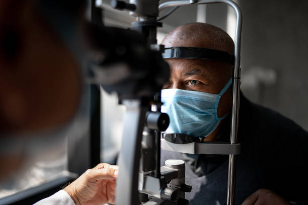 Optometrist examining patient's eyes - wearing face mask Optometrist examining patient's eyes - wearing face mask eye exam stock pictures, royalty-free photos & images