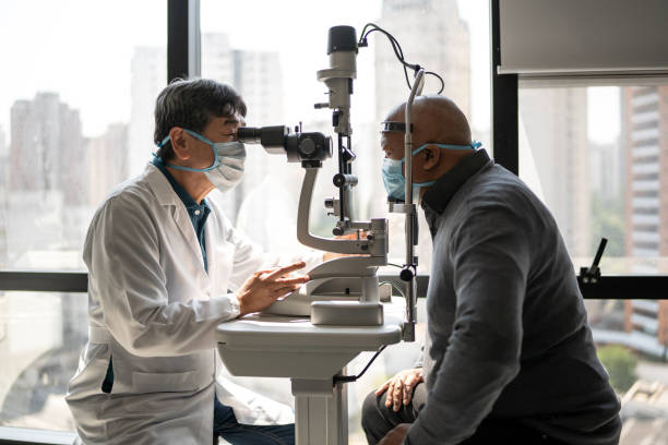 Optometrist examining patient's eyes - wearing face mask Optometrist examining patient's eyes - wearing face mask eye surgery photos stock pictures, royalty-free photos & images