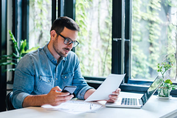 sérieux pensif réfléchi réfléchi axé sur le jeune entrepreneur occasionnel propriétaire de petite entreprise comptable comptable au bureau regardant et travaillant avec des ordinateurs portables et des documents de déclaration de revenus - comptes épargne photos et images de collection