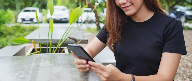 Closeup image of a young asian woman holding and using mobile phone in the outdoors