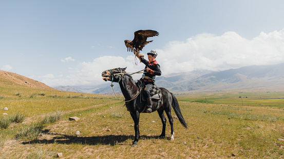Eagle Hunter in traditional costume riding horse with Golden Eagle in the mountains of Central Asia