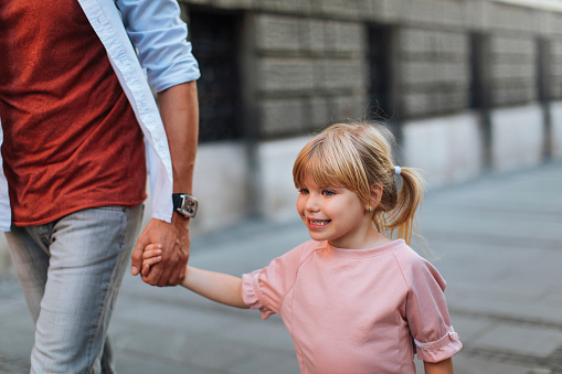 Little blond girl holding her fathers hand while walking down the street