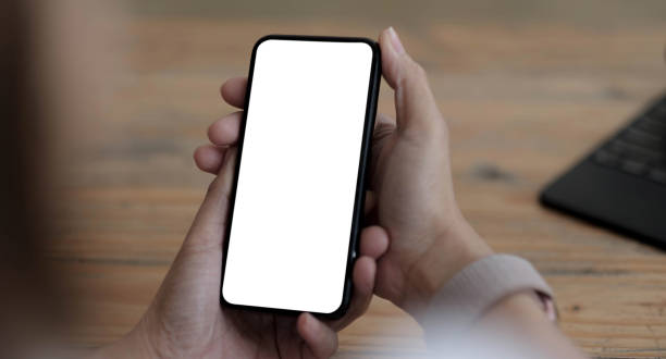 istock Mockup image blank white screen cell phone.women hand holding texting using mobile on desk at home office. 1343835448