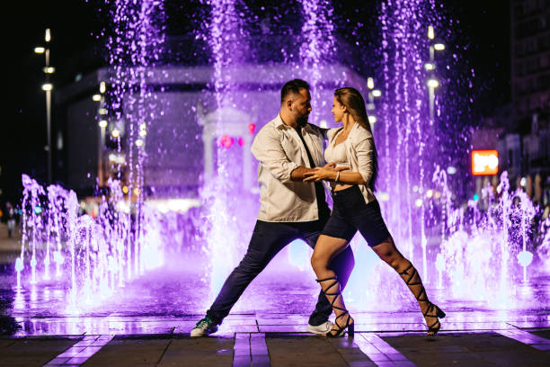 молодая пара танцует рядом с красочным фонтаном - dancing fountains стоковые фото и изображения