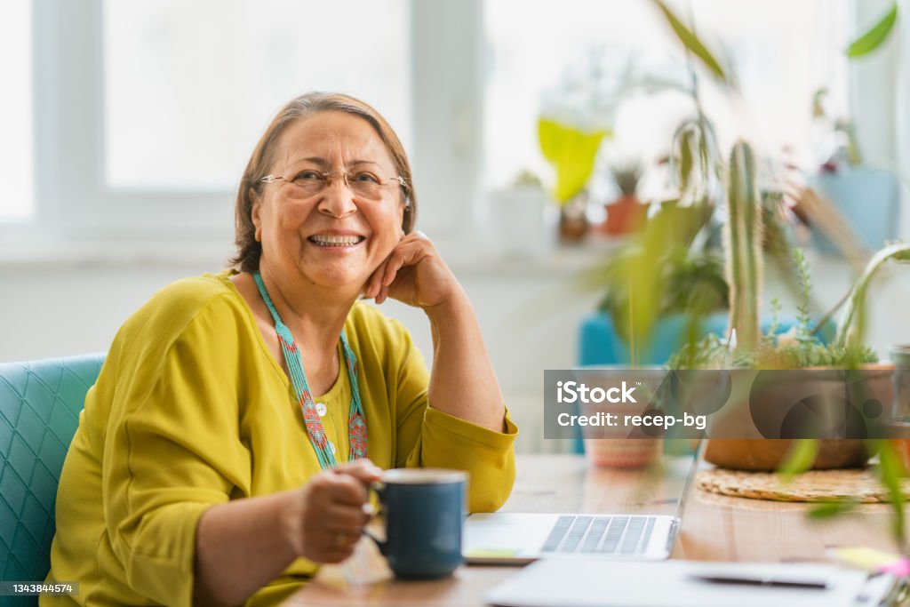 Portrait of happy fashionable senior woman smiling for camera while using laptop at home A portrait of a happy fashionable senior woman smiling for the camera while using a laptop at home. Senior Adult Stock Photo