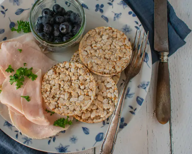 Fresh and homemade healthy and gluten free breakfast plate with thin sliced chicken breast, brown rice cakes and fresh blueberries. Closeup and isolated view from above