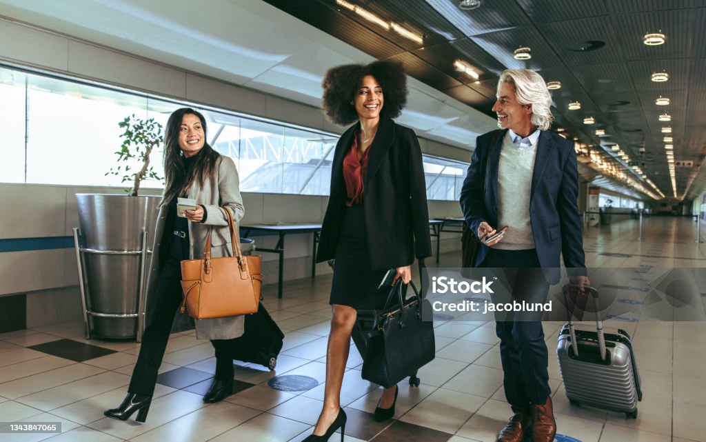 Multi ethnic people going on business trip Group of multi-ethnic business people going on business trip carrying suitcases while walking through airport passageway. Business Travel Stock Photo