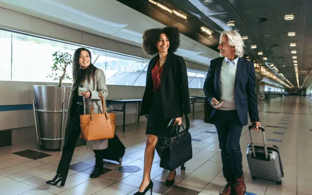 Group of multi-ethnic business people going on business trip carrying suitcases while walking through airport passageway.