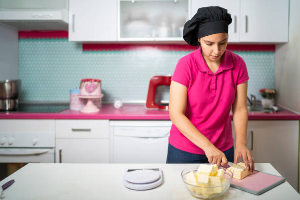 uma mulher corta manteiga para fazer creme de confeiteiro para fazer um bolo - baking cake making women - fotografias e filmes do acervo