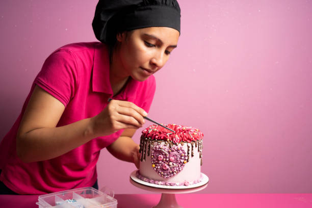 frau, die den rosa kuchen dekoriert, den sie zubereitet hat - konditor stock-fotos und bilder