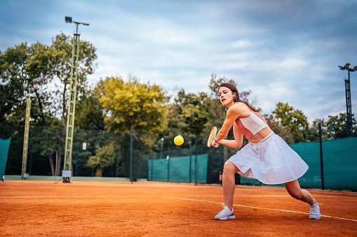 Young female tennis player on the court hitting the ball