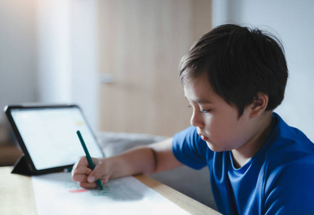 istock Portrait Schoolboy using colour pen drawing on white paper sheet, Young kid using tablet for school homework online on internet, Happy child enjoy painting. Home Education 1343855575
