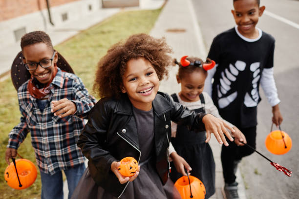 Carefree Children on Halloween Group of smiling African-American kids trick or treating outdoors and walking to camera holding pails trick or treat stock pictures, royalty-free photos & images