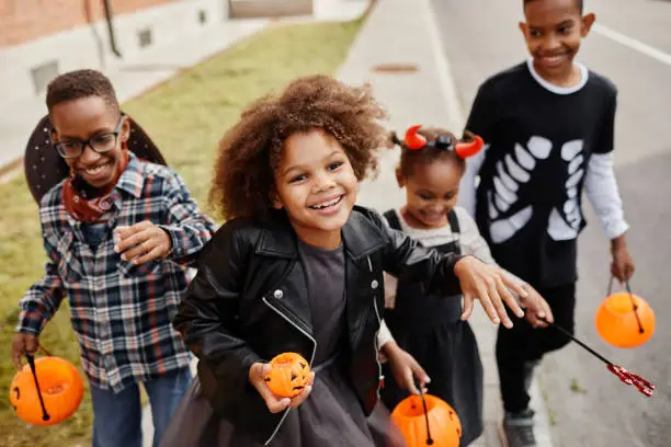 Group of smiling African-American kids trick or treating outdoors and walking to camera holding pails