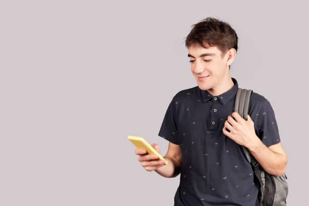 istock A young student wearing casual clothes, texting with his smartphone while carrying backpack isolated on gray background. Copy space 1343859305