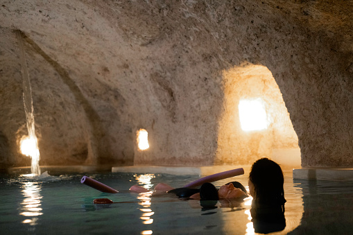 Hispanic masseuse provides an aquatic floating massage to a guest in warm water inside a salt cave  cenote pool below the inn, Valladolid, Yucatan, Mexico