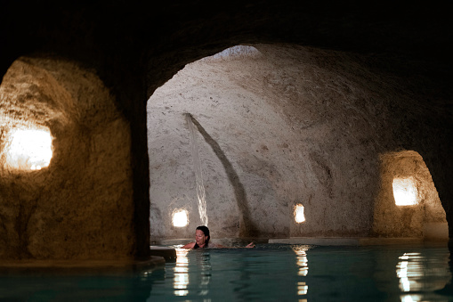 Female guest relaxes under the massaging  waterfall in the warm water of the salt cave cenote pool below the inn,  Valladolid  Yucatan  Mexico