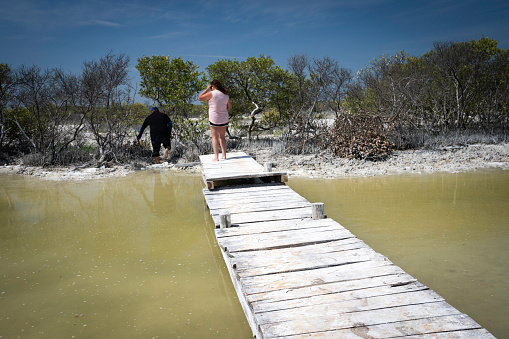 Female tourist follows her Hispanic guide barefoot across a wooden boardwalk to reach squishy mud flats in the nature reserve, Yucatan, Rio Lagartos, Mexico