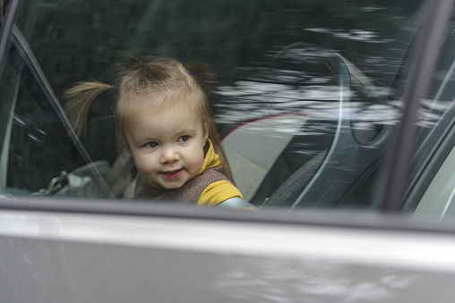 Cute and lovely toddler girl, sitting on a backseat, looking through a car window