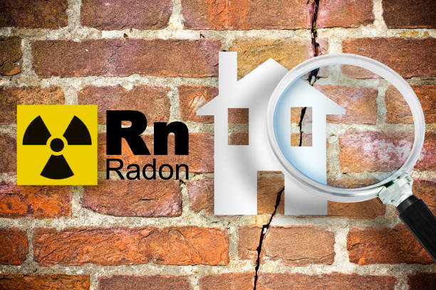 The danger of radon gas in our homes - concept with periodic table of the elements, radioactive warning symbol and home silhouette seen through a magnifying glass against a cracked brick wal stock photo