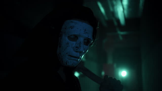 Maniac in mask holding axe portrait, standing in dark corridor. Mystical scary murderer going to kill, carrying murderous weapon. Halloween costume of killer. Horror scene or nightmare concept