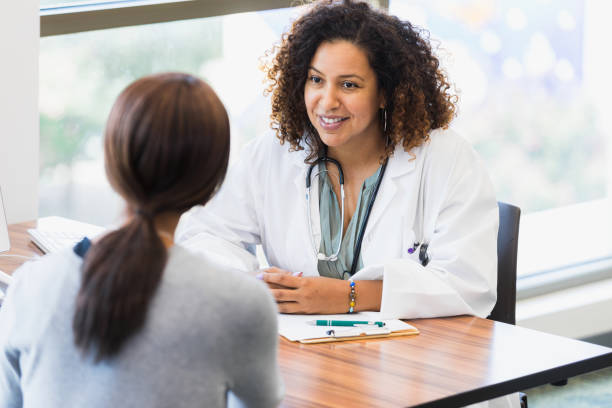 mid adult female doctor listens attentively to unrecognizable female patient - womens issues imagens e fotografias de stock