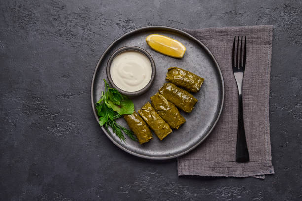 dolma plat, persil, casserole avec crème sure et citron dans une assiette noire sur une table sombre - sour taste green traditional culture lemon photos et images de collection