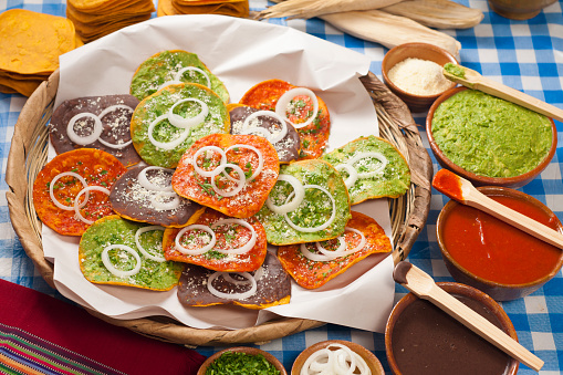 Guatemalan tostadas in a basket with manila paper and some tomato, guacamole, and black bean sauces on the side.