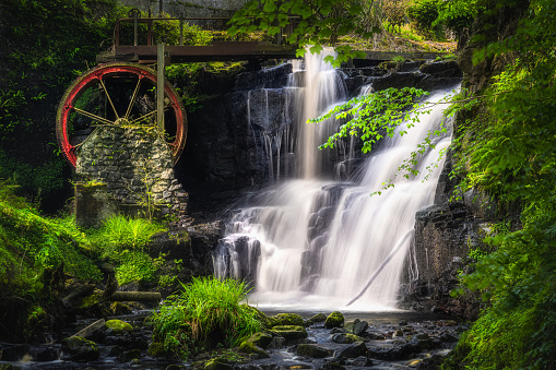 Vintage red waterwheel with waterfall at spring in Glenariff Forest Park, County Antrim, Northern Ireland. Long exposure and soft focus photography