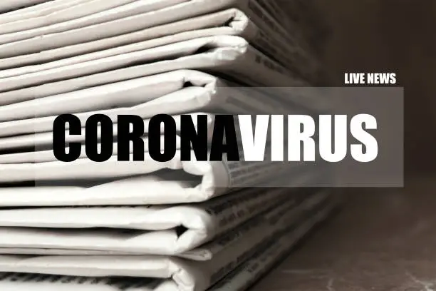 Photo of Word CORONAVIRUS and stack of newspapers on table, closeup. Journalist's work