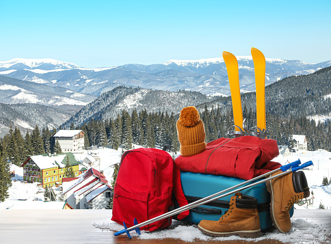 Suitcase with warm clothes on wooden surface against beautiful mountain landscape