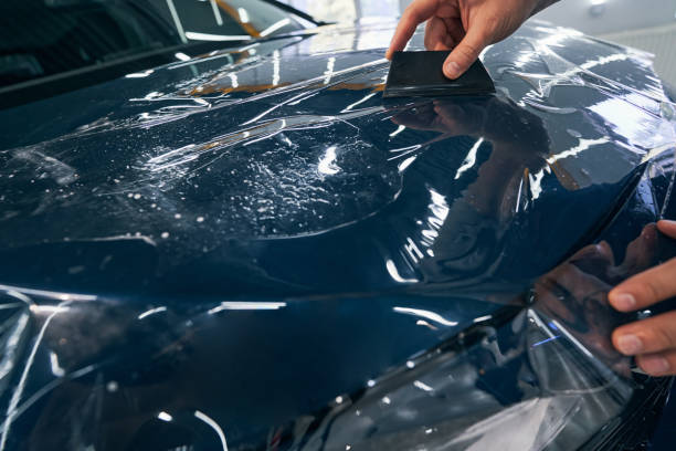 istock Auto service technician installs protective film with squeegee on hood 1343904595