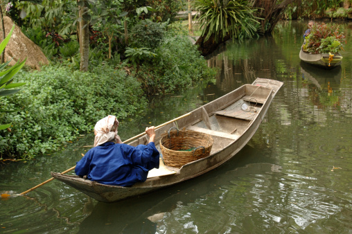 Elderly Thai woman rowing her boat to market on a canal outside Bangkok, Thailand