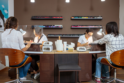 Two young female manicurists working in a nail salon, giving nail treatment to customers
