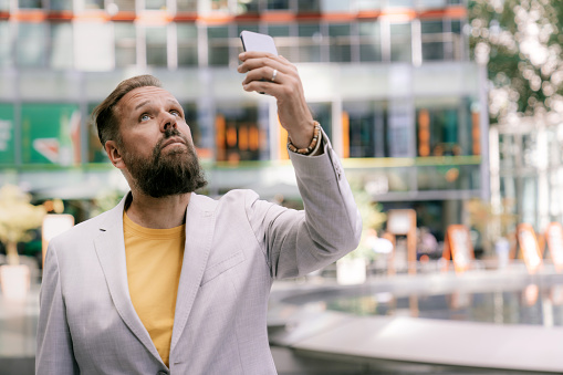 Shot of a mature businessman searching mobile network in the city. Male executive holding his mobile phone high outdoors and looking for the network.
