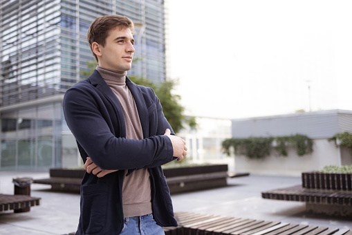 A side view portrait of a successful young Caucasian businessman confidently standing outside of a office building, and looking away in the distance