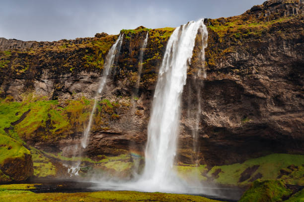 Famous Seljalandsfoss Waterfall on a windy under windy overcast moody cloudscape. The waterfall is around 60m high and is part of the Seljalands River which has its origin in the volcano glacier Eyjafjallajökull. Seljalandsfoss, Route 1, Southern Iceland, Iceland, Nordic Countries, Europe