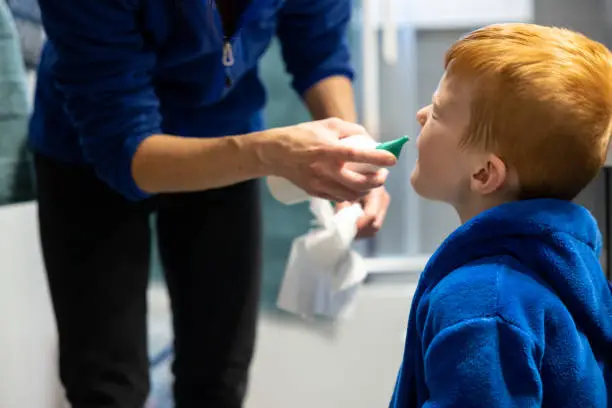 Mother Cleaning and Emptying her Son's Nose With Saline Nasal Spray. The child is holding the saline nasal spray and blowing his nose. During the Covid-19 pandemic, it is important to avoid the spread of the virus and to take care of each other.