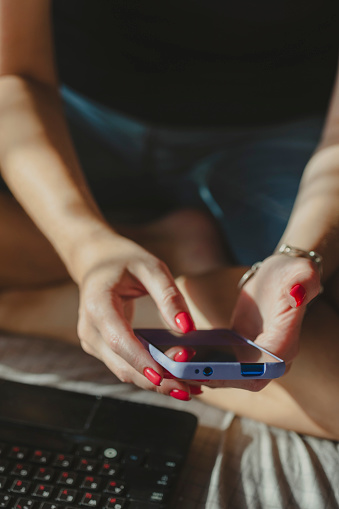 Young millennial woman texting on mobile device. Hands of a woman wearing bright red nail polish in frame, closeup. Online shopping concept.
