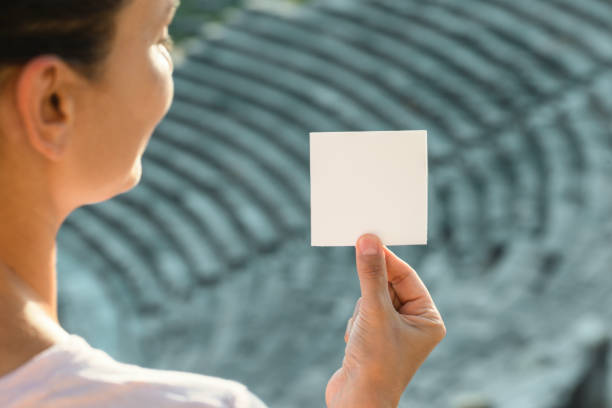 Over the shoulder view of an unrecognizable caucasian female standing in an amphitheater and is looking at blank white note in her hand. Steps of the theater are visible in the background.