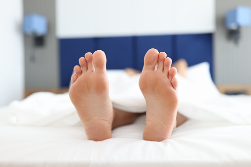 Female feet lying on white bed under covers closeup. Insomnia treatment concept