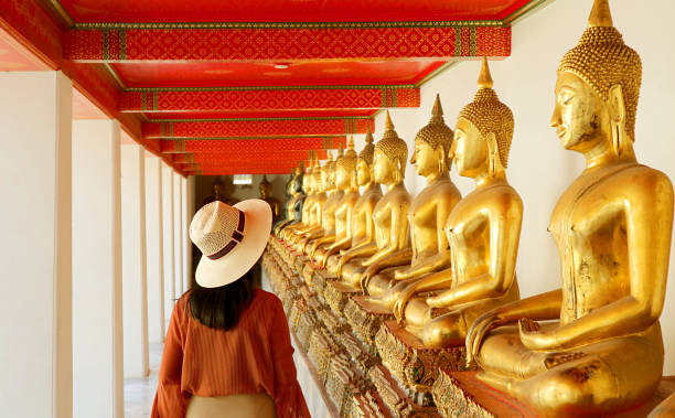 mujer visitando el claustro con un gran grupo de imágenes de buda sentado en el templo wat pho, ciudad vieja de bangkok, tailandia - bangkok fotografías e imágenes de stock