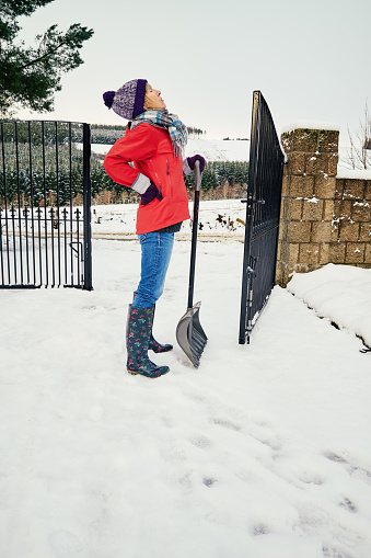 Senior woman has backache from clearing snow from her front yard with a snow shovel.