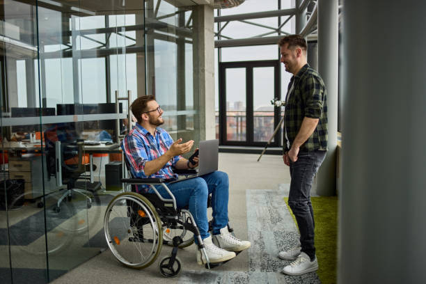 istock Disabled computer programmer discussing with male coworker in office hallway 1343999050