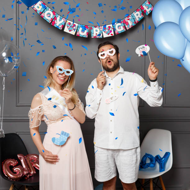 Happy couple holding balloons with inscription boy or girl during gender reveals party, over colored confetti and balloons. stock photo