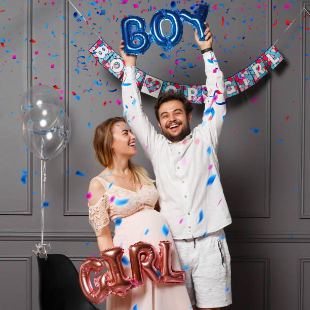 Happy couple holding balloons with inscription boy or girl during gender reveals party, over confetti and balloons. stock photo