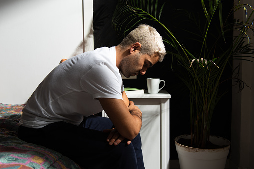 Depressed hispanic man sitting on his bed thinking on his problems. Stress, anxiety, depression and mental health concept.