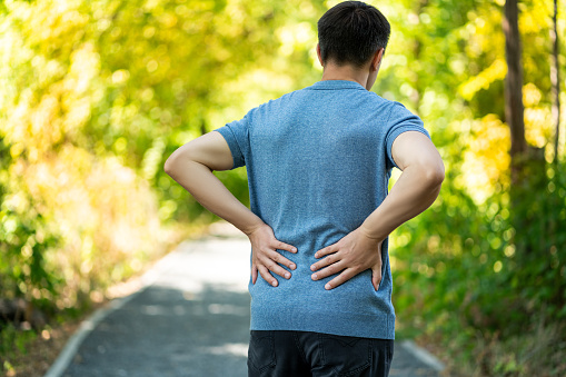 Back pain when walking outdoors, man with kidney inflammation on nature background, health problems concept
