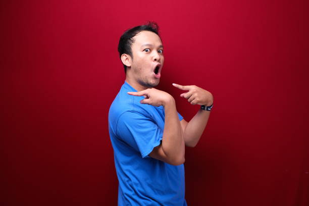 istock Young asian man is surprised and shouting wow with pointing right with his hand isolated on red background. 1344008744